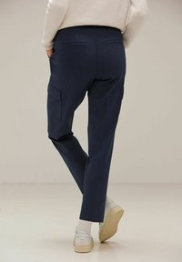 Pantalons cargo navy au design ajusté, dotés de poches latérales, texture lisse et taille mi-haute, associés à des baskets blanches et des chaussettes.
