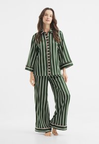 Conjunto de pijama a rayas verdes que incluye una camisa de botones con mangas de 3/4 y pantalones de pierna ancha, acentuado con detalles en rojo y blanco.