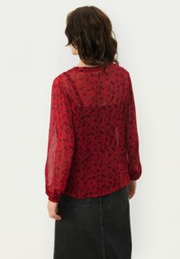 Blusa de flores rojas con mangas largas y transparentes, y escote redondo. La tela parece ligera y semitranslúcida.