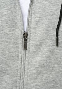 Sivi dukserica na zip s metalnim zatvaračem, koja ima oznaku na povlačenju, uže i teksturiranu tkaninu.