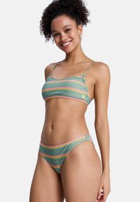 Grøn bikini med striber, der har tynde stropper og en lav talje. Striberne er i pink, gul og blå; blød tekstur med en let glans.