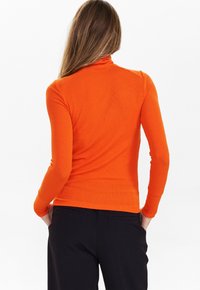 Col roulé ajusté à manches longues en tissu côtelé orange vif, associé à un pantalon noir. Texture lisse, design minimaliste, dos sans coutures.