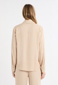 Koszula z długim rękawem i kołnierzykiem, w pionowy wzór beżowo-kremowych pasków. Posiada mankiety na guziki i luźny krój o gładkiej teksturze.