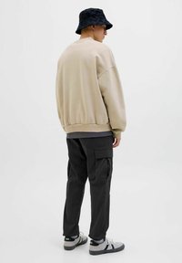 Beige übergroßer Sweatshirt, schwarze Cargo-Hosen und ein schwarzer Bucket Hat. Der Sweatshirt hat gerippte Bündchen, die Hosen besitzen seitliche Taschen.