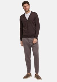 Dunkelbrauner Cardigan mit V-Ausschnitt und Knopfschluss, kombiniert mit hellgrauen taillierten Hosen und braunen Slippern.