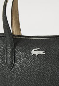 Black textured leather handbag with a silver crocodile logo, top zipper closure, and tan interior lining. Short, structured handles.