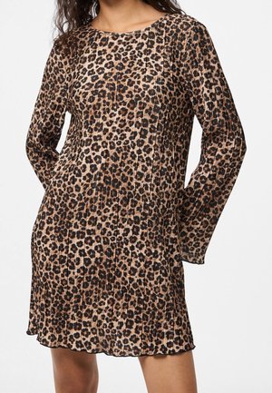 Kobieta ubrana w długą sukienkę z długim rękawem w panterkę z plisami i okrągłym dekoltem, stojąca z rękami za plecami.