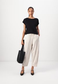 Top nero a maniche corte, pantaloni larghi a righe crema, mules neri con tacco e borsa a tracolla nera. Design minimalista e stile casual.