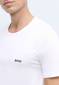 Valge puuvillane T-särk, millel on ümar kaelus ja lühikesed varrukad. Rinnal must broderitud "BOSS" logo. Sile tekstuur.