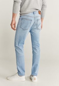 Jeans de mezclilla azul claro con un corte ajustado, que presentan dos bolsillos traseros y una etiqueta de cuero marrón en la cintura, combinados con zapatillas blancas.