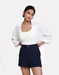 Weißes, knopfbares Hemd, eng anliegendes weißes Tanktop und dunkelblaue, hoch taillierte Shorts mit vorderen Taschen und silbernem Knopfdetail.