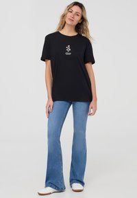 T-shirt in cotone nero con maniche corte, con ricami floreali rosa e il testo "Bloom" sopra. Abbinato a jeans a palazzo blu chiaro.