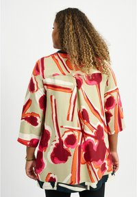 Blusa multicolore con un design floreale in rosso, rosa e arancione su sfondo beige; progettata con maniche a tre quarti e una vestibilità ampia.