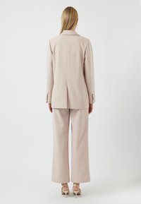 Vaaleanbeige räätälöity puku, jossa on pitkät hihat ja leveät housut. Sileä rakenne, hienovarainen ompeluyksityiskohta ja yksi halkio takana bleiserissä.