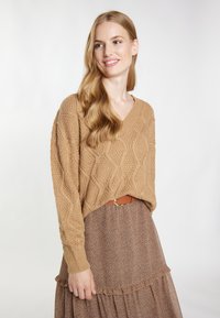 Jasnobrązowy sweter dzianinowy z dekoltem w serek i wzorem rombów, w połączeniu z brązową spódnicą w kwiaty i brązowym paskiem, z detalami falbanki.