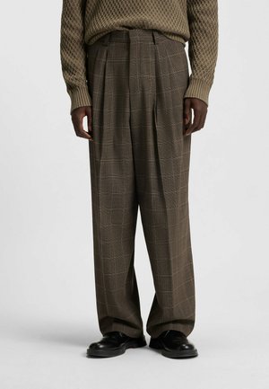 Brown plaid trousers with a loose fit, featuring pleats and a textured fabric, paired with black shoes for a complete look.