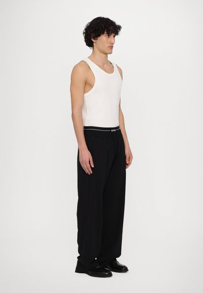 White tank top and black wide-leg trousers. The pants have a drawstring waist and a contrasting brand label on the waistband. Smooth fabric.