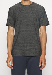 Camiseta deportiva negra hecha de una tela texturizada con un sutil patrón a rayas, que presenta un pequeño logo negro en el lado izquierdo del pecho.