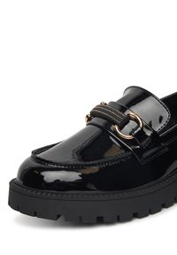 Czarne lakierowane loafersy z grubą czarną podeszwą, z złotym zapięciem i tanowymi akcentami w szyciu.