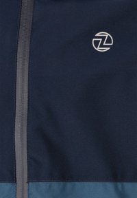 Marineblå zip-up jakke lavet af glat, let stof med en grå lynlås og et diskret logo i det øverste venstre hjørne.