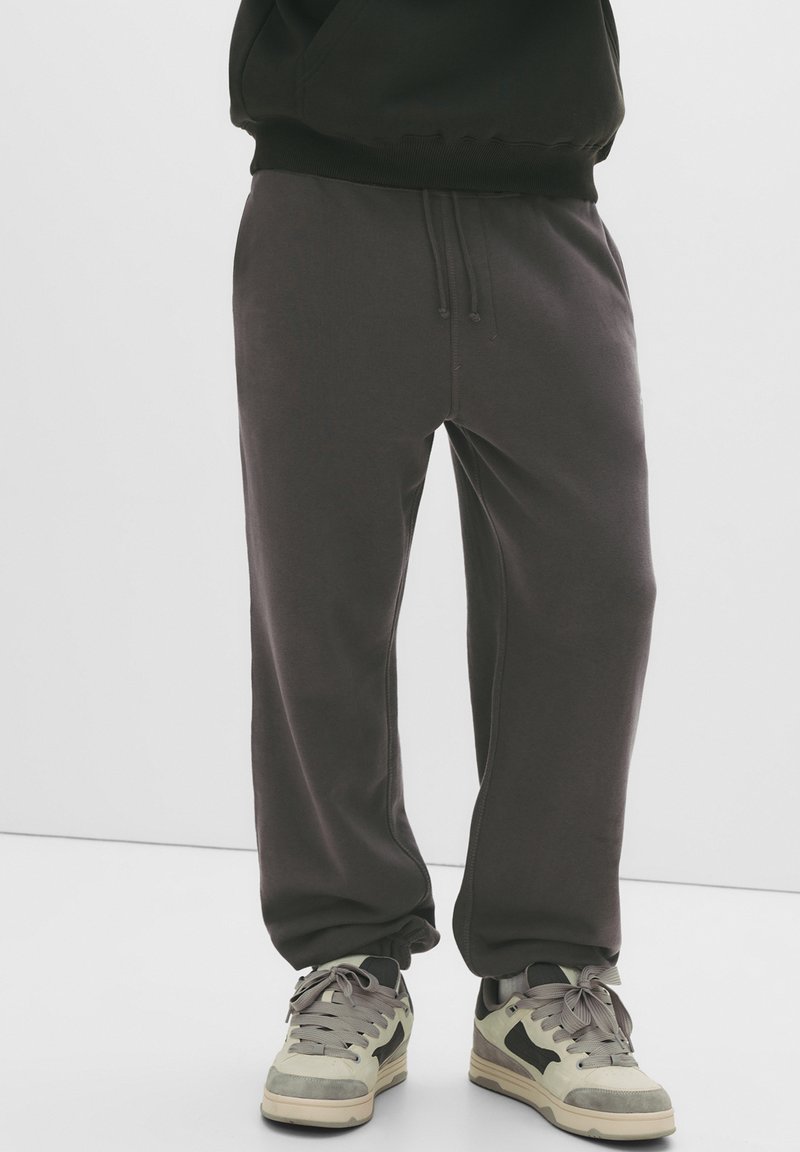 Donkergrijze sweatpants met elastische taille en boorden, gemaakt van zachte stof, gecombineerd met lichtgrijze sneakers met donkere accenten.