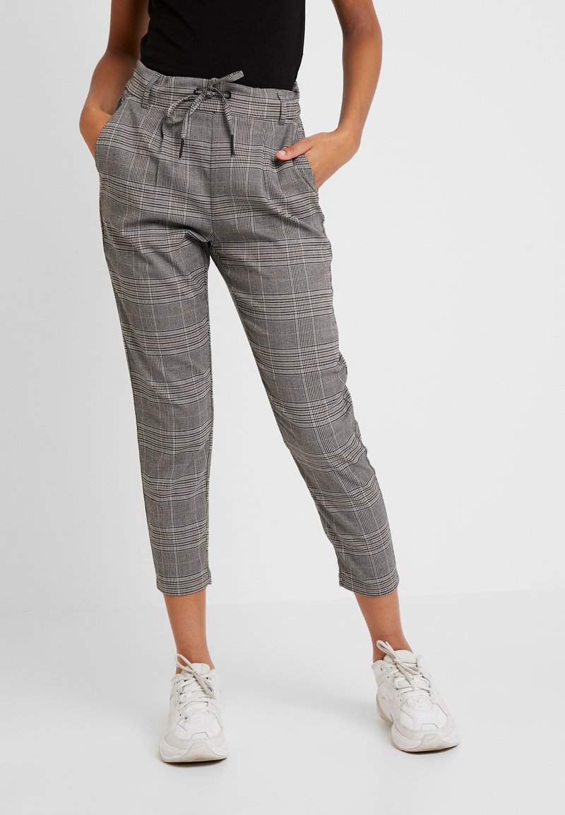 Grå rutiga byxor med elastisk midja och dragsko, med sidofickor och en tapered ben-design, ihop med vita sneakers.