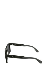 Czarne okulary przeciwsłoneczne z grubą, prostokątną oprawą wykonaną z błyszczącego plastiku. Zauszniki mają delikatne zwężenie i ozdobione są logo.