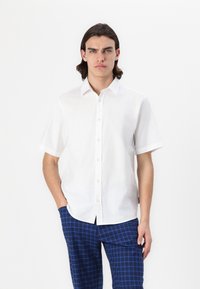 Camicetta bianca in lino a maniche corte con colletto button-down, con una texture liscia e una vestibilità comoda, abbinata a pantaloni a quadri blu.