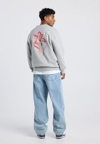 Gray sweatshirt with red floral design on back, paired with light blue baggy jeans and sneakers. Soft fabric, relaxed fit, round neckline.