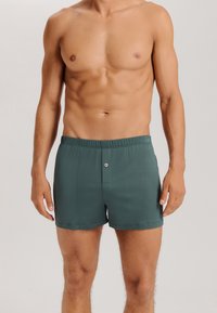Mörkgröna bomullsboxershorts med resår i midjan, framknäppning och en slät yta, sydda så att de passar kroppen.
