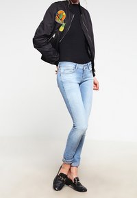 Chaqueta bomber negra con parches bordados, top negro ajustado, jeans skinny de mezclilla azul claro y mocasines negros, con una textura suave.