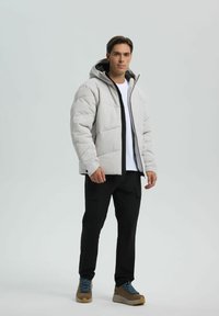 Hellgraue gepolsterte Jacke mit Kapuze, schwarzem Reißverschluss und seitlichen Taschen. Kombiniert mit schwarzen Cargo-Hosen und beigen Wanderschuhen.