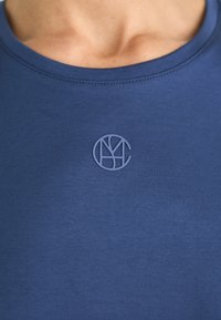 Marineblauw t-shirt met een gladde textuur, voorzien van een klein, reliëf rond logo op de borst, dat een minimalistisch ontwerp toont.