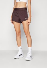 Shorts de sport marron avec des rayures latérales blanches et une ceinture élastique. Associés à des chaussettes et des chaussures blanches, avec des accents noirs.