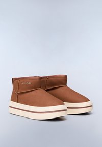 Botas de tobillo marrones con parte superior de imitación de cuero suave, punta redondeada, costado elástico y suela de goma crema con una franja de acento marrón.