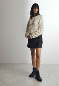 Creme farvet kabelstrikket sweater med lange ærmer, parret med en sort miniskørt og sorte snørebånds combat støvler. Glatte teksturer og lagdelt look.