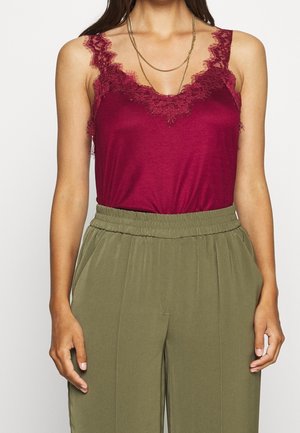 Vinröd linne med spetsdetaljer vid halsringningen, kombinerat med olivgröna höga byxor med elastisk midja.