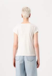 Kurzärmliges weißes T-Shirt mit rundem Halsausschnitt, glatter Textur und lässiger Passform, kombiniert mit hellblauen Jeans.