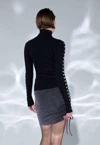 Schwarzes Rollkragenoberteil mit gerippter Textur und silbernen Knöpfen an den Ärmeln, kombiniert mit einem taillierten grauen metallischen Minirock.