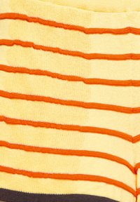 Tissu tricoté jaune avec des rayures orange horizontales et un ourlet noir en bas, montrant la texture et le contraste des couleurs.