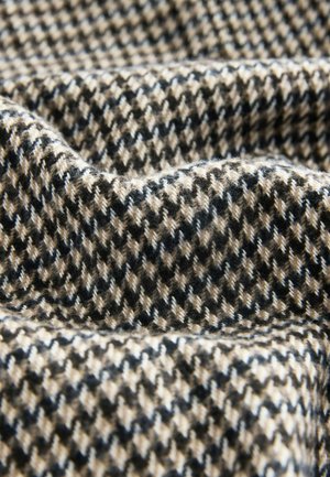 Struktureret stof med et hundetænder-mønster i sort, beige og hvidt, med bløde, let fuzzy fibre og en draperet fremtoning.