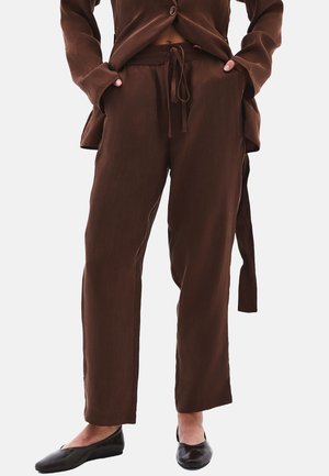 Braune, leichte, lässig geschnittene Hosen mit Gummizugbund und seitlichen Taschen; kombiniert mit schwarzen flachen Schuhen. Glatte Textur und gerades Bein-Design.