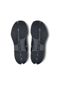 Les semelles extérieures des chaussures de sport noires présentent un caoutchouc textur�é avec un motif de grip, y compris une rainure centrale et une semelle variée pour une meilleure traction.