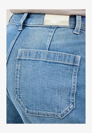 Lyseblå denimjeans med en baglomme og et mærke med teksten "LIPSY LONDON" ved taljen. Materialet ser ud til at være struktureret med syningsdetaljer.