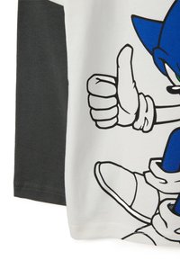 Camiseta de manga corta con un personaje de dibujos animados azul sobre un fondo blanco y una manga negra. Tejido de algodón, diseño simple, impresión gráfica.
