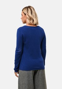 Královsky modrý svetr s kulatým výstřihem a dlouhými rukávy, vyrobený z měkké látky. Zadní část je přiléhavá a hladká, v kombinaci se šedými kalhotami s širokými nohavicemi.