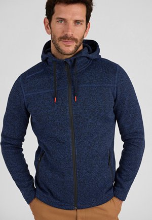 Chaqueta de forro polar azul marino con cremallera frontal, cuello alto y capucha ajustable. Presenta extremos de cordón naranja y dos bolsillos laterales con cremallera.