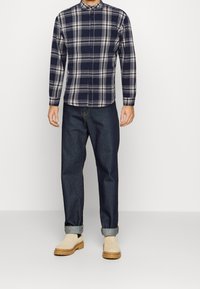 Camicia a quadri in blu navy e grigio, maniche lunghe, design con bottoni. Abbinata a jeans blu scuro, con risvolti, e stivali beige con suole in gomma.