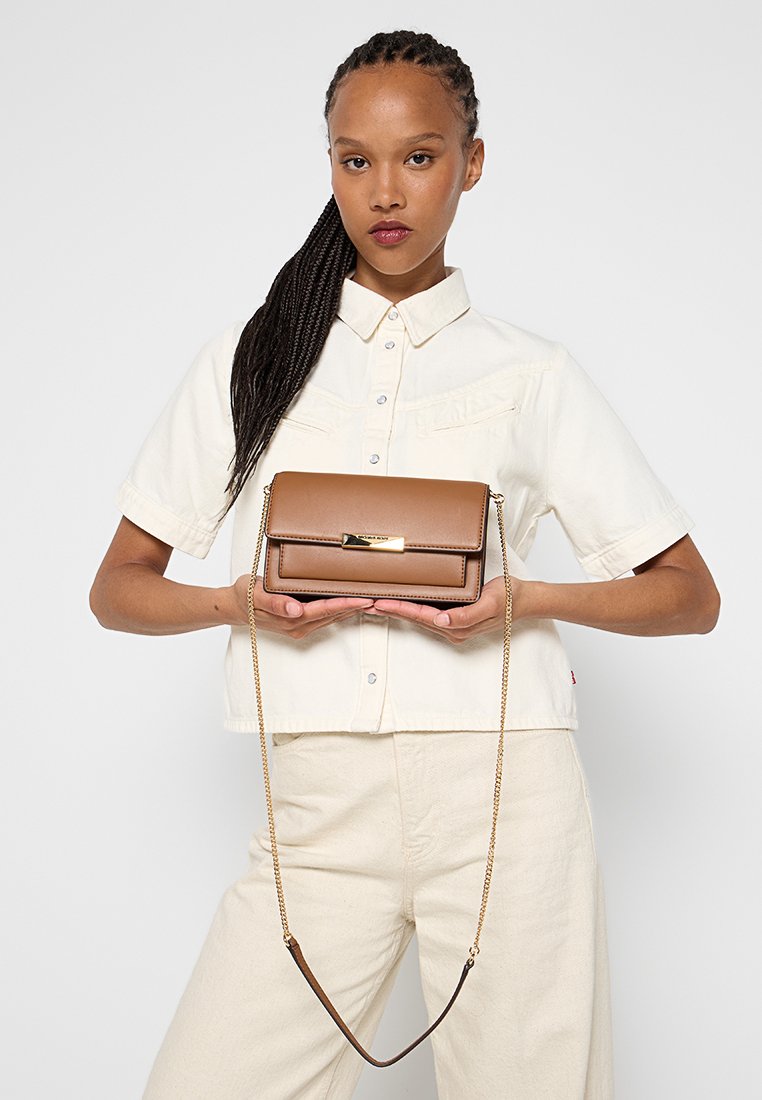 Sac à main en cuir marron avec une chaîne en or, présentant une forme rectangulaire et un détail de fermoir à l'avant. Texture lisse avec un design élégant.