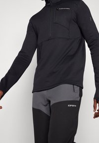 Zwarte lange mouwen kwart-rits pullover van gestructureerde stof, met een voorkantzak en contrasterende grijze accenten. Draag het met aansluitende grijze en zwarte broeken.